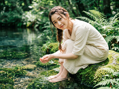 美しい森の透き通る川で水をすくい優しく微笑む女性
