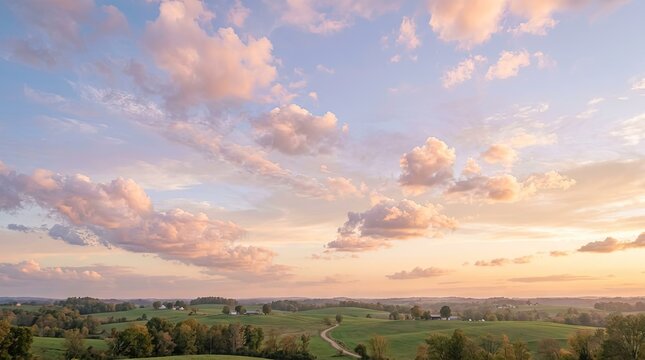 A panoramic view of a rural landscape at sunset, featuring rolling green fields, scattered farmhouses, and a vibrant sky with soft, pastel clouds.