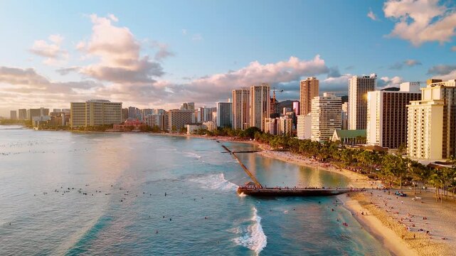 Aerial view of Waikiki beach with surfer, Honolulu, Hawaii. Turquoise wave, sandy shore, pier and hotel tower at golden hour.