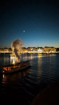 Historic steam boat cruising on the Binnenalster lake in Hamburg at twilight with Christmas tree and city skyline illumination.