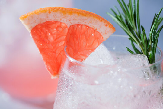 Close-up of a refreshing pink grapefruit cocktail with ice, fresh rosemary, and a juicy grapefruit wedge garnish.Vibrant macro food photography, restaurant menus, cocktail bars, healthy beverages