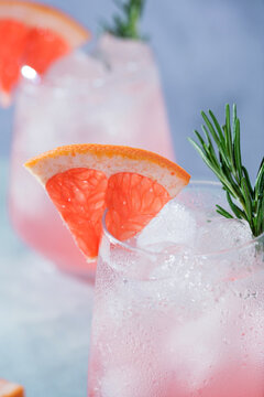 Close-up of a refreshing pink grapefruit cocktail with ice, fresh rosemary, and a juicy grapefruit wedge garnish.Vibrant macro food photography, restaurant menus, cocktail bars, healthy beverages
