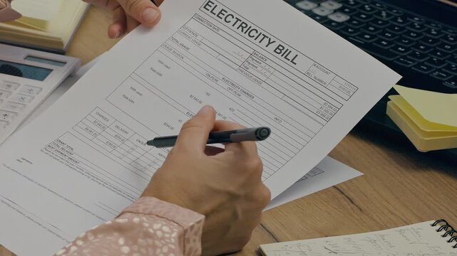 Woman calculating and 
verifying electricity, household utility bills at home office, writing down calculations