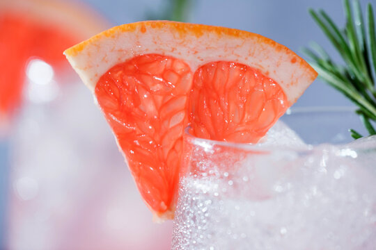 Close-up of a refreshing pink grapefruit cocktail with ice, fresh rosemary, and a juicy grapefruit wedge garnish.Vibrant macro food photography, restaurant menus, cocktail bars, healthy beverages