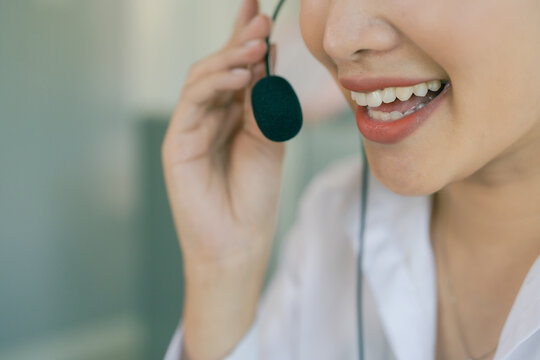 A smiling Asian female call center agent wearing a headset and speaking with a customer, set against an office background.