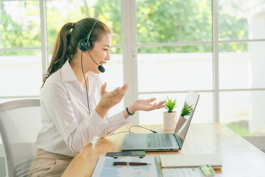 A smiling Asian female call center agent wearing a headset and speaking with a customer, set against an office background.