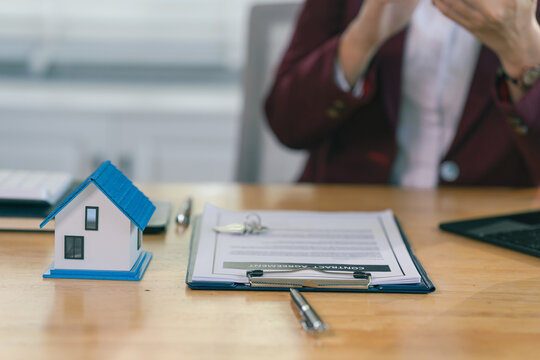 An Asian female client is signing a real estate purchase agreement with an agent who is explaining the contract details to the homebuyer.