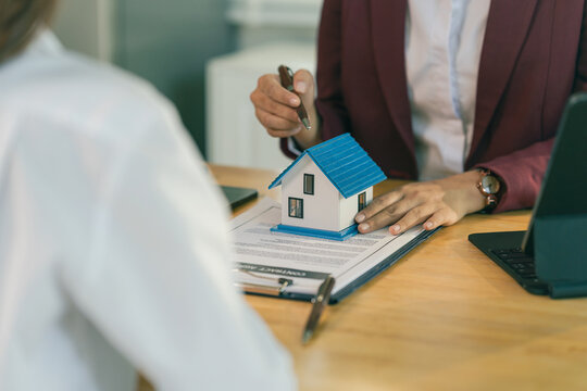 An Asian female client is signing a real estate purchase agreement with an agent who is explaining the contract details to the homebuyer.