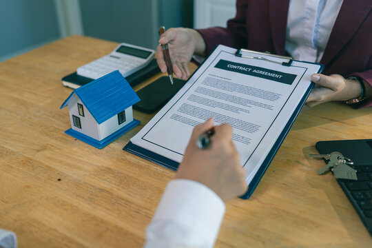 An Asian female client is signing a real estate purchase agreement with an agent who is explaining the contract details to the homebuyer.