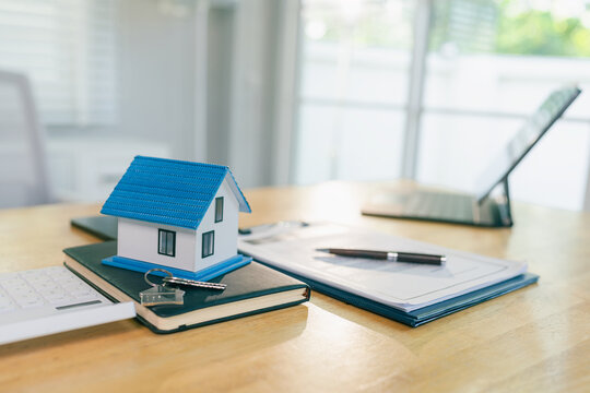 Small house model with keys and contract document on office wooden desk.Real estate contract with pen, house model, and laptop computer on table.