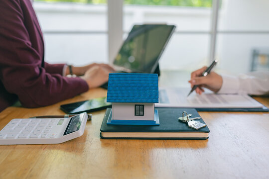 An Asian female client is signing a real estate purchase agreement with an agent who is explaining the contract details to the homebuyer.