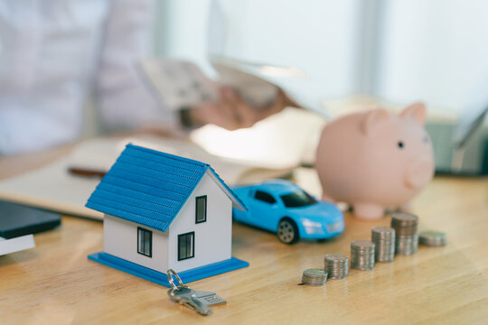 Smiling Asian woman putting coin into piggy bank for house saving concept