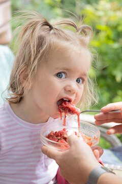 toddler girl, one and a half years old, opens her mouth wide, getting ready to eat a spoonful of delicious borscht. Daily routine. Mom is spoon-feeding the child.