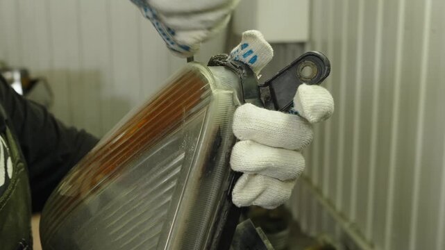 A mechanic in work gloves repairs a car headlight assembly.