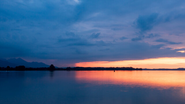 Fiery sunset beneath dramatic storm clouds over Lake Chiemsee, Bavaria, Germany