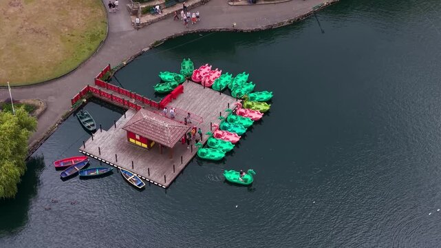 Aerial footage of colourful dragon pedal boats moored at the Peasholm Park jetty with visitors enjoying the boating lake in the popular seaside resort of Scarborough North Yorkshire England