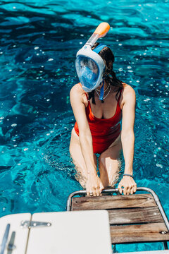 Woman in a red swimsuit and snorkel mask climbs onto the wooden swim platform of a boat. Boat charter leisure and snorkeling excursions for summer sea travel and watersport rental