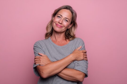 Warm self-hug portrait: everyday woman expresses self-acceptance against soft pink background