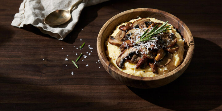 Creamy polenta topped with sauteed mushrooms and rosemary in wooden bowl mushrooms rosemary vegetarian delicious homemade nutrition vegetable parmesan lighting background culinary