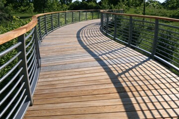 Obraz premium Curved wooden walkway with metal railings under bright sunlight