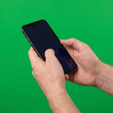Hands holding a black smartphone on green background