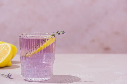 Refreshing lavender lemonade served in elegant ribbed glasses with fresh lavender sprigs and a lemon twist. Light purple citrus drink on a soft pastel background