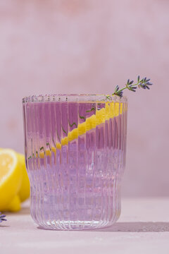 Refreshing lavender lemonade served in elegant ribbed glasses with fresh lavender sprigs and a lemon twist. Light purple citrus drink on a soft pastel background