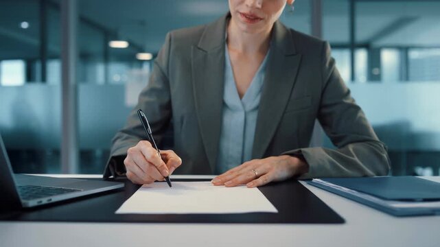 Professional businesswoman signing documents at modern office desk with laptop and files