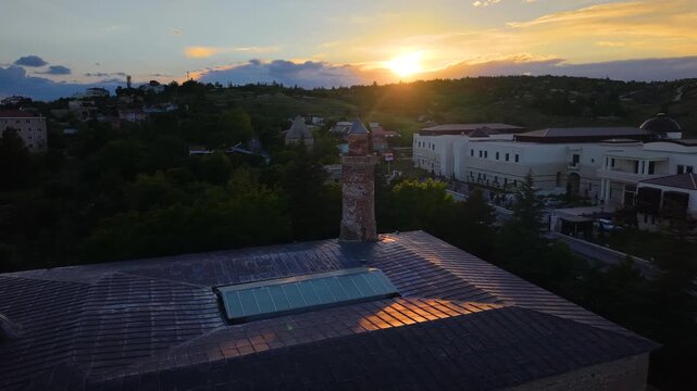 4K cinematic drone slowly approaches the historic Harput Ulu Mosque at sunset, passing above the mosque while revealing its iconic minaret against a glowing golden sky.