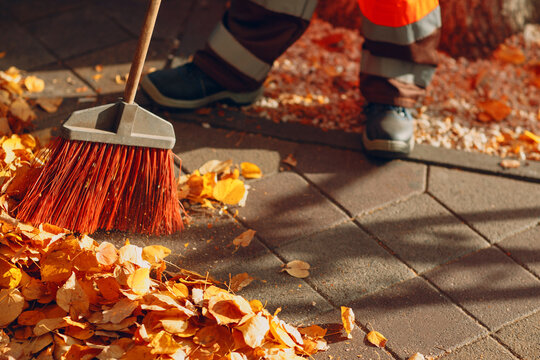 Janitor cleaner sweeping off autumn leaves and garbage trash on the street walkway.