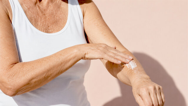 senior woman applying moisturizing body lotion on her arm. Skin care and anti-aging routine for mature female. Beauty treatment, hydration, solar protection and health wellness concept