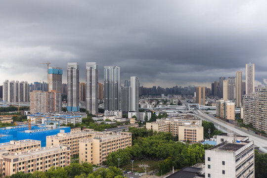 Aerial view of Wuhan city, the capital of Hubei, China. Dramatic storm clouds hang over a dense urban skyline of modern high-rise apartments, construction cranes and an elevated highway