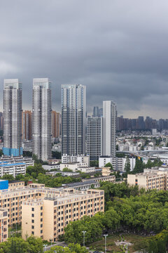 Vertical bird eye view of Wuhan city, the capital of Hubei, China. Dramatic storm clouds hang over a dense urban skyline of modern high-rise apartments, construction cranes and an elevated highway