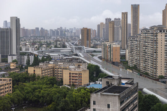Aerial view of Wuhan city, the capital of Hubei, China. Rainy clouds hang over a dense urban skyline of modern high-rise apartments, construction cranes and an elevated highway