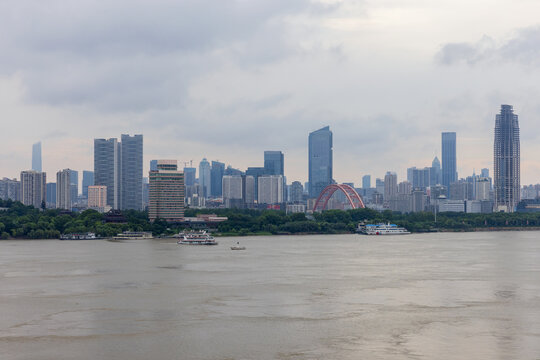 Wuhan city skyline along a wide river featuring a red arch bridge, passenger boats and high-rise buildings, conveying modern city life, river transport, waterfront architecture and skyline views