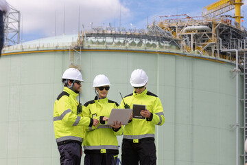 Fototapeta premium Engineers collaborating on construction project at industrial site with laptop and tablet in hand under blue sky