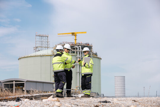 Engineers discussing project plans at a construction site with industrial equipment in the background