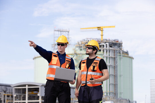 Two engineers discussing construction plans at a modern industrial site with safety gear and equipment