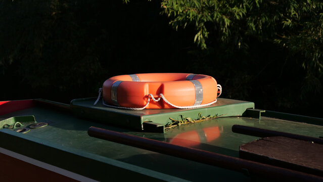 Lifebuoy on canal boat roof, orange life ring with reflective tape, safety equipment, boat deck, sunny day, river background, reflections, safety first