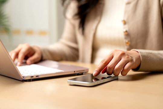 Close up hand of woman point or touch on mobile phone screen during work with laptop.