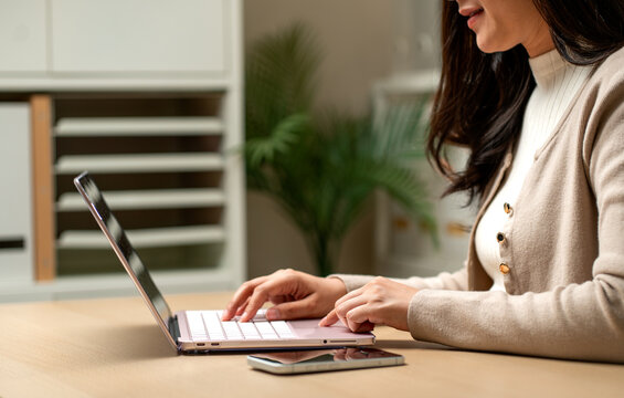 Side view of woman work with laptop and use finger to move cursor for working and she also smile with happiness during work.