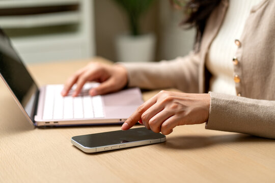 Side view close up hand of woman point or touch on mobile phone screen during work with laptop.