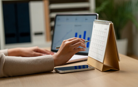 Close up hand of woman use pen to point on the calendar on table during use laptop for working in concept of the success day for business.