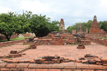 Fototapeta premium Ancient Temple Ruins in Thailand: Timeless beauty of ancient brick temple ruins in Thailand, set against a backdrop of lush green trees and a cloudy sky. A testament to history and cultural heritage.