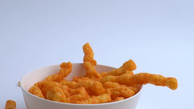 close up of cheese corn puffs being dropped from above into a white plastic bowl