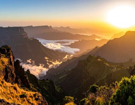 Sunrise over majestic mountain peaks, casting long shadows and illuminating clouds.