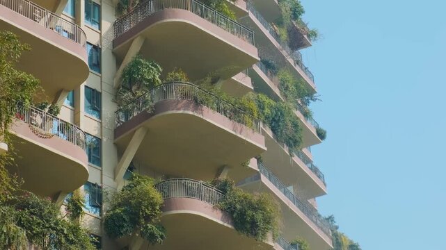 Modern residential building with lush green plants growing on balconies in Chengdu city, China. Close up. Vertical garden, green architecture, eco-friendly city design and future urban sustainability