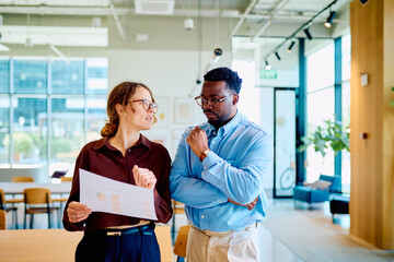 Two diverse business people collaborating, analyzing document data, having a discussion in a modern office environment © we.bond.creations