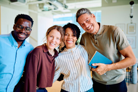 Diverse business colleagues posing together, smiling and embracing, showing teamwork, friendship and success in a modern office
