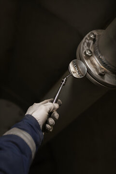 Gloved industrial worker hand holding telescopic articulated inspection mirror examining metal pipe flange weld joint inside confined space, visual corrosion inspection procedure
